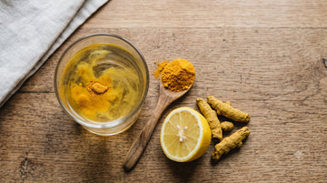 Turmeric powder settling in a glass of water for a home purity test, next to a lemon and whole turmeric root